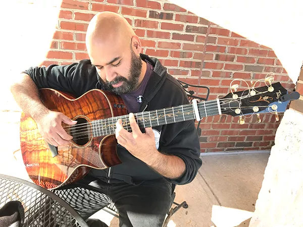 Banda sits at Mugs Coffee, picking the custom Taylor acoustic he named Ele.