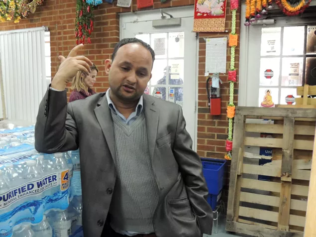 Kamal Dhimal speaks from inside his store (above), where a stone that was thrown through the window last night still lies (below). - RYAN PITKIN